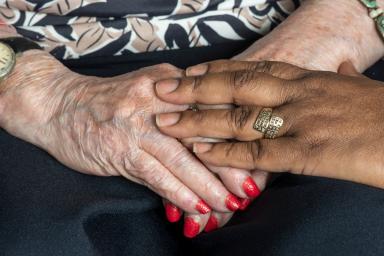A close up of two women's hands - one woman has her hands in her lap while the other woman pats her hand.