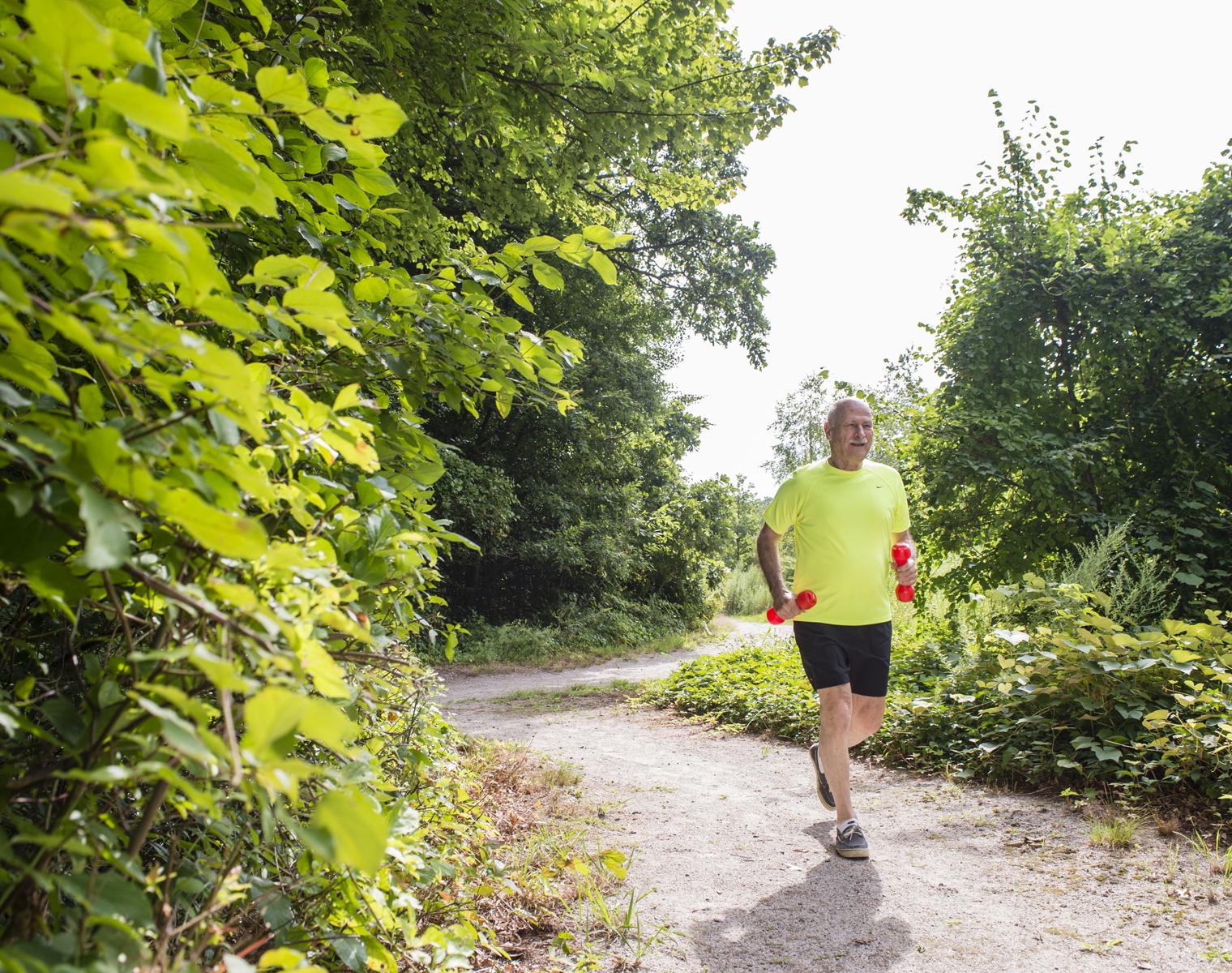 A resident of NewBridge on the Charles jogs with hand weights through one of the wooded trails that surround the community.