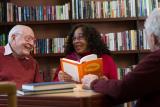 Three seniors converse around a table in a library.