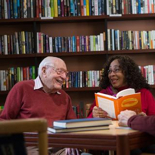 An older man and woman converse about a book in a library.