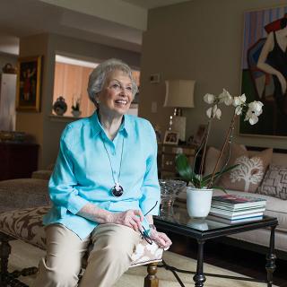 A smiling older woman sits in her apartment.