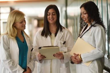 A group of three female fellows stand together and look at a file