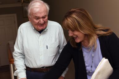 A Home Health worker smiles while helping a male patient with his walker 