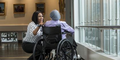 A female caregiver bends down to talk to a patient in a wheelchair