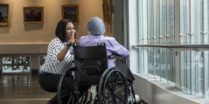 A female caregiver bends down to talk to a patient in a wheelchair 