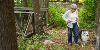 An elder woman walks a dog on one of Hebrew SeniorLife's walking trails