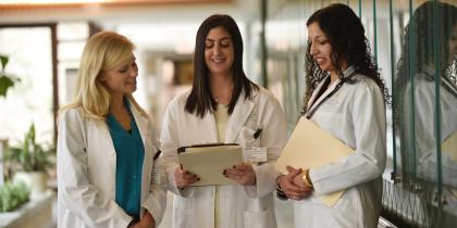 A group of three female fellows stand together and look at a file