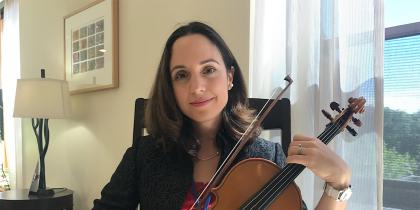 NewBridge on the Charles employee, Leticia Alvaraz, plays a violin while smiling 