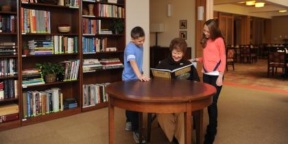 A woman resident sits in a library and reads a book with two children