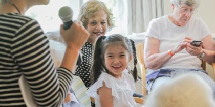 a young girl wearing braids looks up and smiles while a woman speaks into a microphone