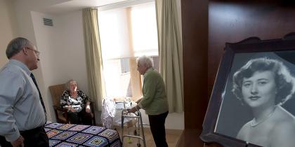 Hebrew SeniorLife's CEO Lou Woolf stands near a residents bed while talking to her and a female friend 