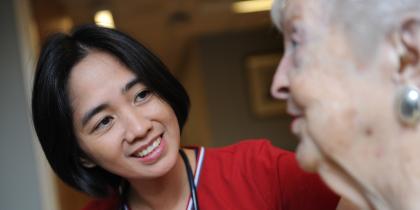 A female nurse in red scrubs sits and talks with a female resident 