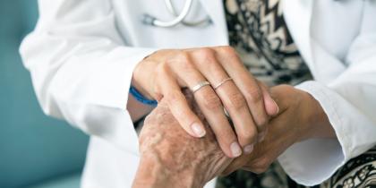 A female doctor wearing a white coat places her hand over a patient's hand 