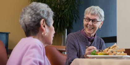 Two female friends laugh while enjoying a meal together