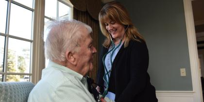 A Home Health worker smiles while checking a male patient's blood pressure