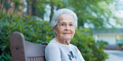 Woman with glasses and serious expression sitting on bench outside.