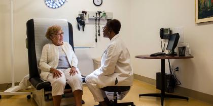 Doctor sitting on stool speaks with elderly patient in an examining room