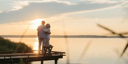 senior couple standing in front of a sunset by the water