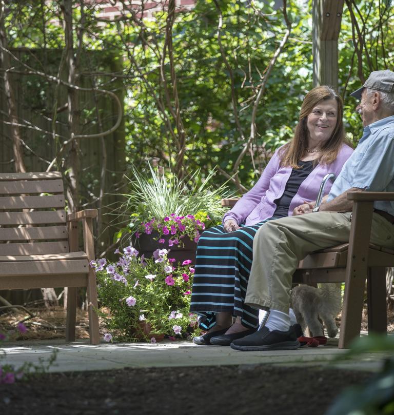 A man and woman sit on a bench in an outdoor garden area.