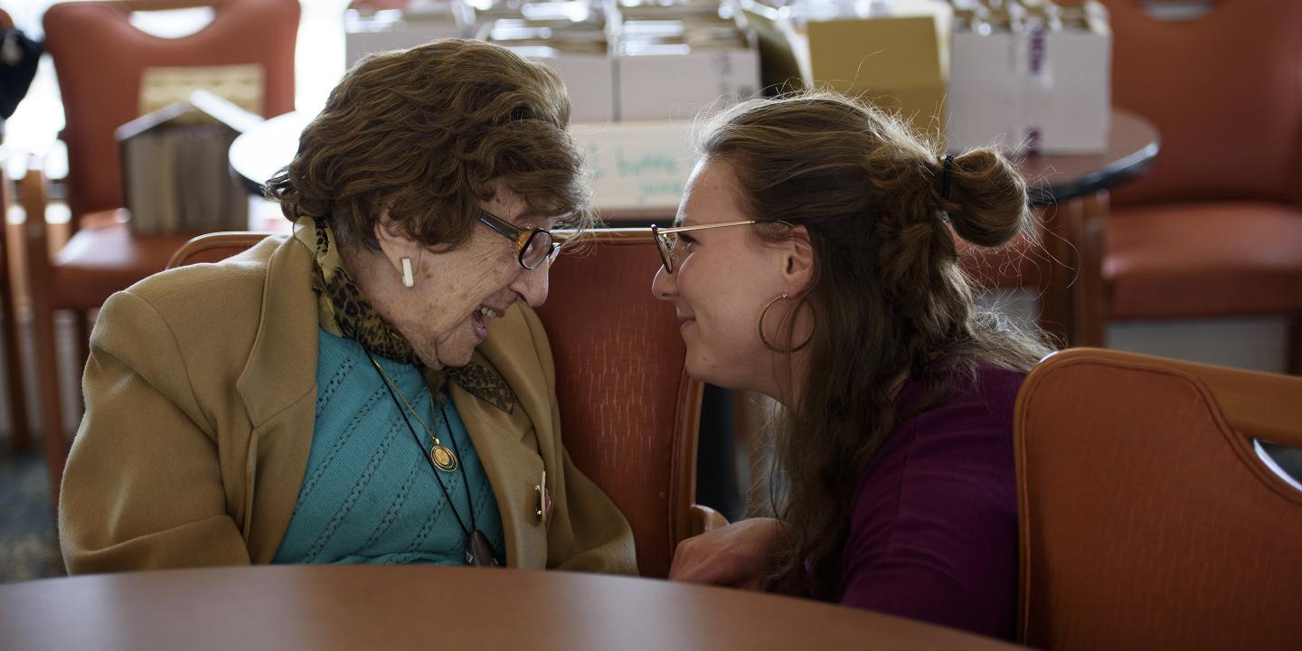 Young woman kneels down to talk to an older woman at Hebrew Rehabilitation Center