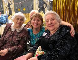 A smiling nurse puts her arms around two Russian-speaking patients at an event.