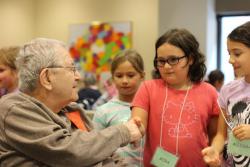 An older man shakes the hand of a school-aged girl and another young girl and boy look on.