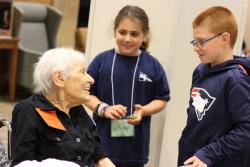 An older female smiles as she looks up at a school-aged boy and girl who are smiling back at her.