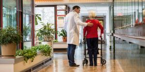 Doctor walking with older woman using a walker