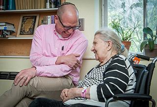 Chaplain sits with white-haired woman, laughing together