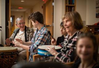 A group of young students participate in a drumming circle with seniors.