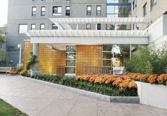 Orange flowers and green shrubs line the entrance to Center Communities of Brookline at 1550 Beacon Street.