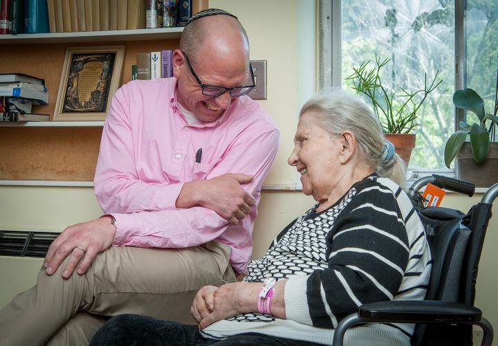 Chaplain sits with white-haired woman, laughing together