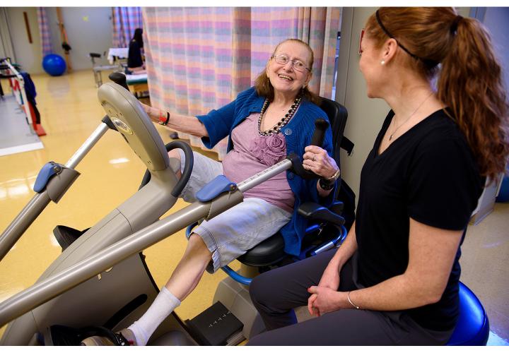 An older woman using a fitness machine with an instructer